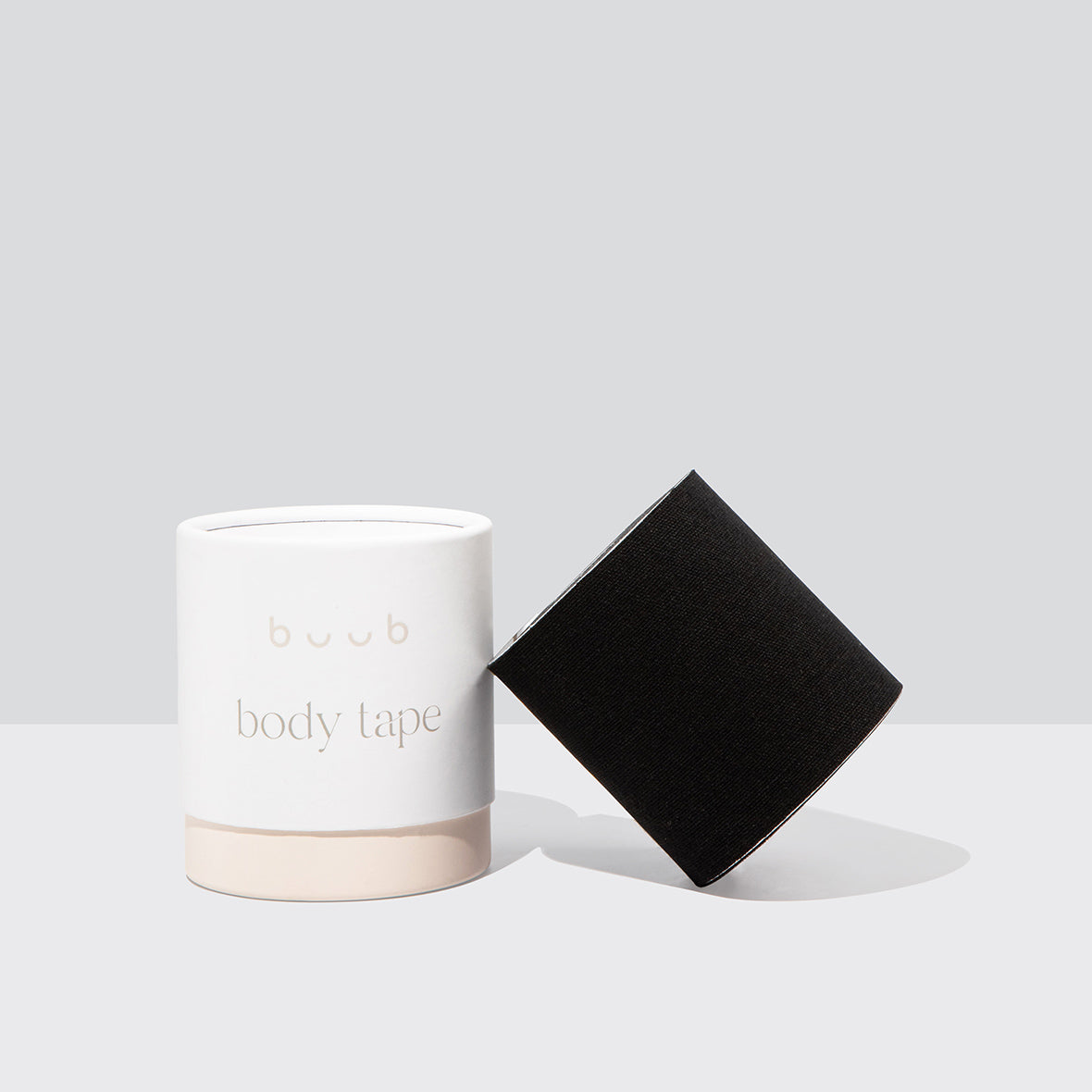A wide roll of Buub Maxi Body Tape in black. This strong-hold breast lift tape is presented with its chic white and beige packaging for a professional product photo.