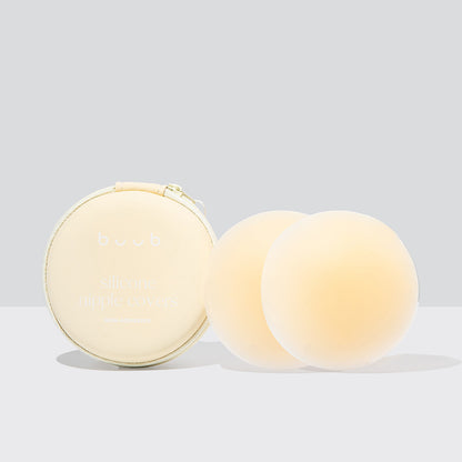A pair of 8cm Buub non-adhesive silicone nipple covers in a light nude shade. The reusable seamless pasties are displayed next to their cream-coloured travel case.