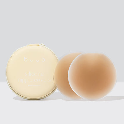 A pair of 10cm Buub non-adhesive silicone nipple covers in a tan shade, shown with their cream-coloured zippered travel case. The reusable pasties offer seamless coverage.